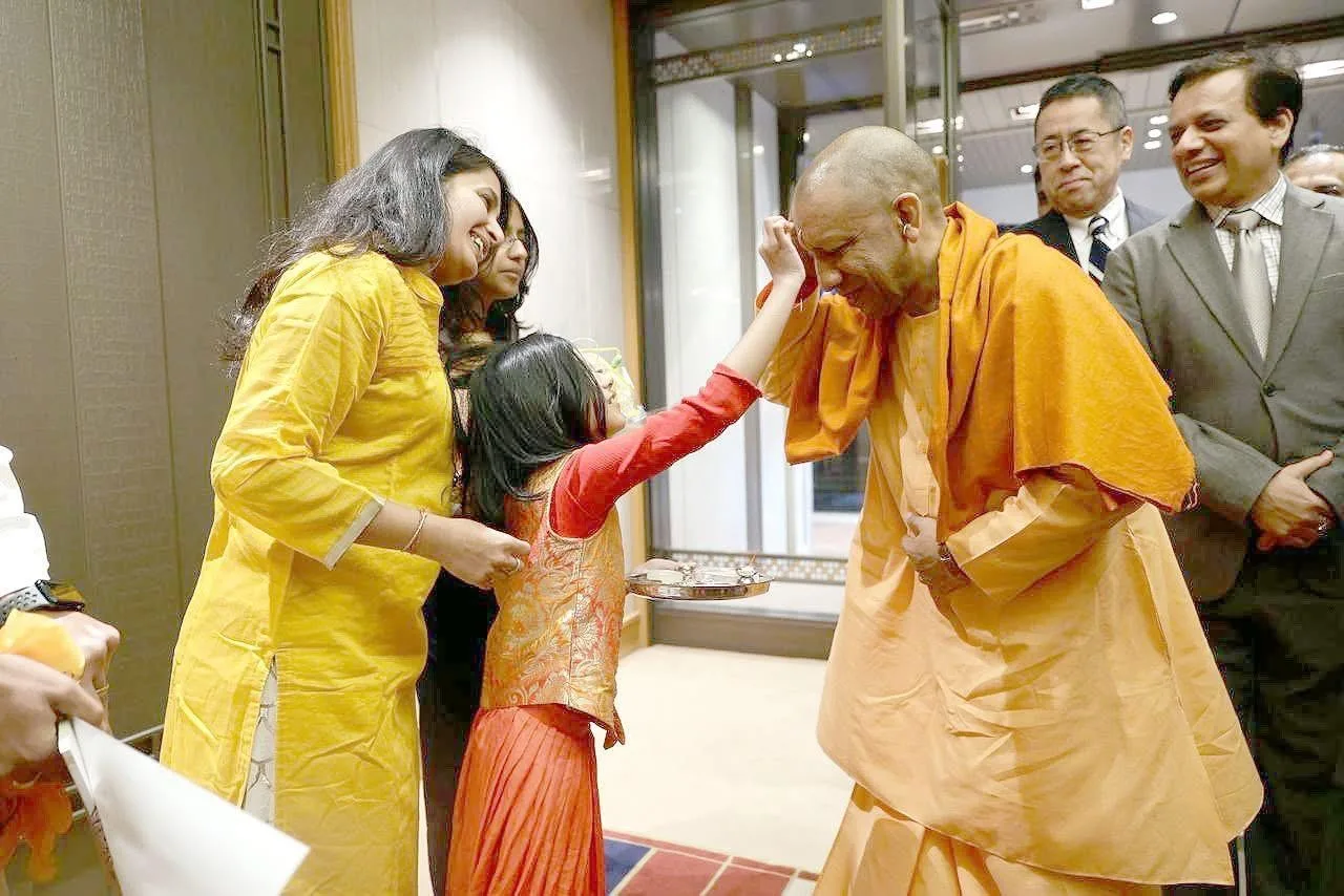A young girl applies a ceremonial tilak to the Chief Minister during a traditional welcome in Japan.